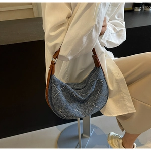 Close-up of blue denim crescent bag featuring silver studs and brown leather strap