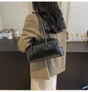 Detail view of the black leather shoulder bag with white contrast stitching on a model