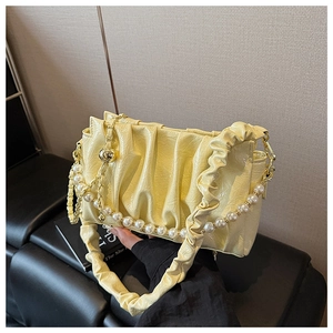 Detailed view of yellow pleated patent leather shoulder bag with a pearl chain strap