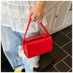 Close-up of red litchi grain leather handbag with pearl lace bow charm held by model