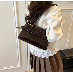 Close-up of deep brown leather shoulder bag with vintage embossed logo on a model