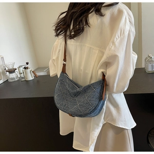 Detail of denim crescent bag featuring silver studs and brown leather strap on model