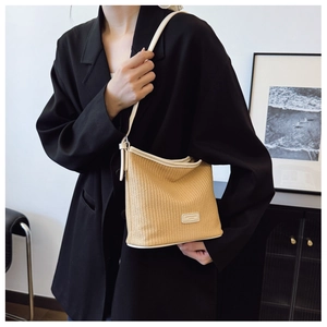 Detail of woven straw bucket bag with beige leather trim and brand logo patch