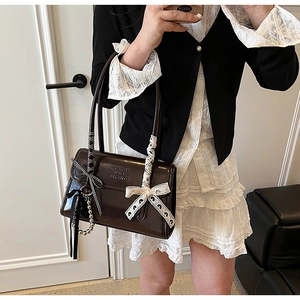 Detail of dark brown glossy patent leather bag with a ribbon bow and pearl charm
