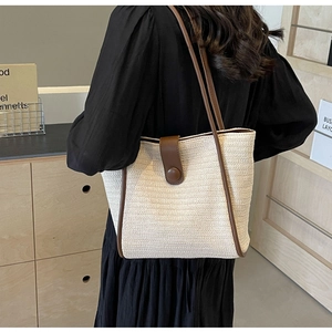 Close-up of woven tote bag with brown leather trim worn by model in a cozy home setting