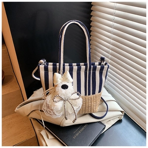 Detail of blue striped canvas tote bag with straw weave base and a plush dog charm