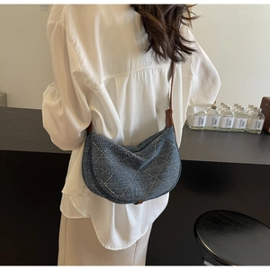 Dettaglio borsa a mezzaluna in denim blu con motivi a rombi borchiati e tracolla in pelle