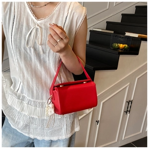 Detail of red leather crossbody bag with gold closure and decorative pearl ribbon charm