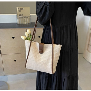 Detail of beige woven tote bag with brown leather straps shown on a model's shoulder