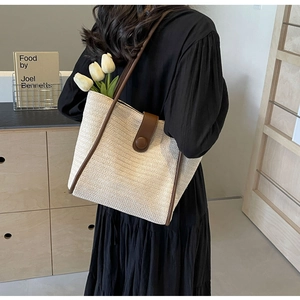 Detail of woven straw tote bag with brown leather trim and white tulips inside