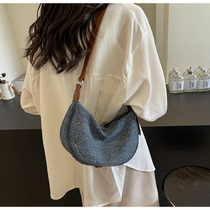 Close-up of denim half-moon bag with silver rivets and leather strap on a model