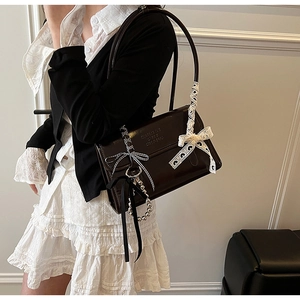 Detail of dark brown leather shoulder bag with decorative bow and heart lace charms