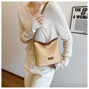 Detail of woven straw bucket bag with brown leather trim and slim shoulder strap