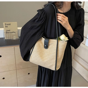 Detail of hand-woven beige straw tote bag with black leather straps and tulip accent