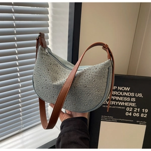 Detail of light blue denim crescent bag with silver studs and adjustable brown strap