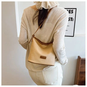 Detail of woven straw bucket bag with dark brown leather trim and adjustable shoulder strap