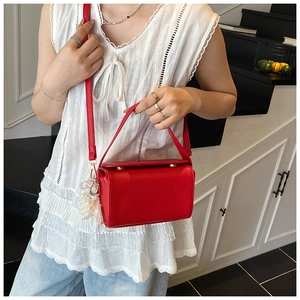 Detail of red lychee leather crossbody bag with pearl and tassel charms on white outfit