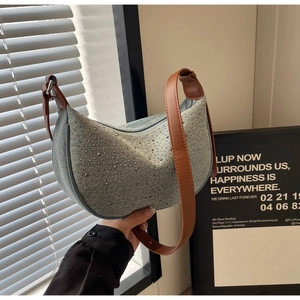 Detail of light blue denim half-moon bag with silver rivets and brown leather strap