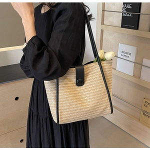 Close-up of woven straw tote bag with black leather trim and magnetic snap button