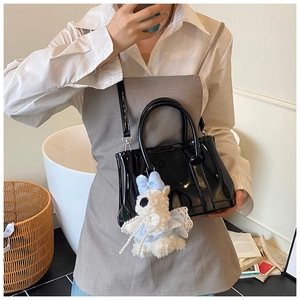 Détail d'un sac seau en cuir verni noir brillant avec breloque chiot en peluche blanche