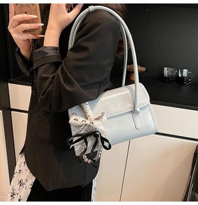 Detail of light blue leather shoulder bag featuring side checkered bow charm on a model