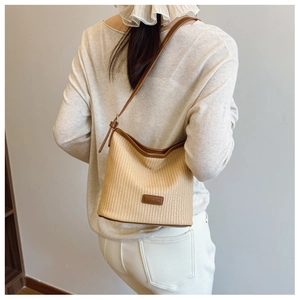 Detail of woven beige shoulder bag with brown leather trim and adjustable strap