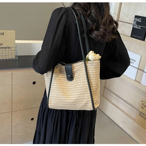 Detail of woven straw tote bag featuring black leather trim and round buckle closure