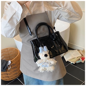 Détail du sac seau en cuir verni noir brillant avec breloque d'ours porté par un mannequin