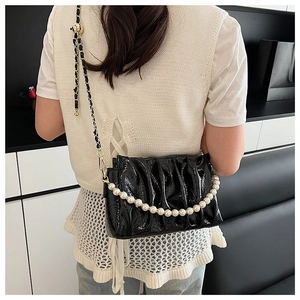 Detail of black pleated cloud bag with glossy finish and white pearl chain strap