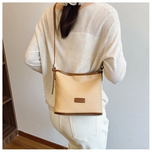 Detail showing the back view of a woven straw shoulder bag with brown leather trim on model