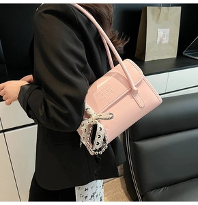 Detail view of pink glossy leather crossbody bag with letter embossing and bow charm
