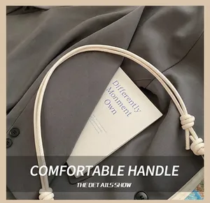 Close-up of cream woven shoulder bag strap with knotted detail and stylish prop card