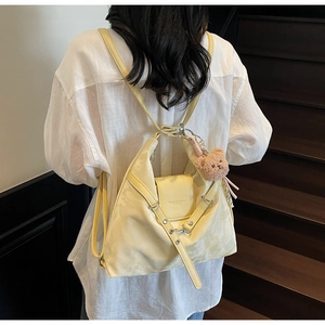 Detailed view of cream yellow convertible backpack featuring a plush bear charm on straps
