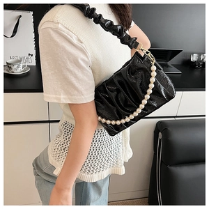 Detail of black pleated cloud bag featuring glossy finish and elegant pearl chain strap