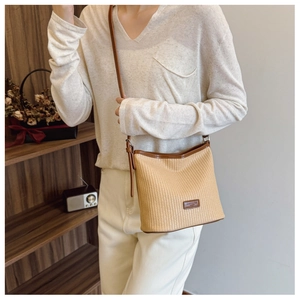 Detail of woven straw shoulder bag with leather logo tag and adjustable brown strap