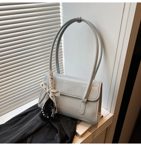 Detail of light blue crossbody bag with embossed logo and polka dot scarf decoration