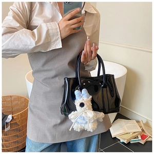 Détail du sac seau en cuir verni noir brillant avec un pendentif ours en peluche blanc