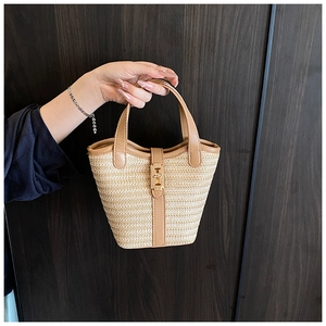 Detailed close-up of woven straw bucket bag with brown leather trim and golden buckle