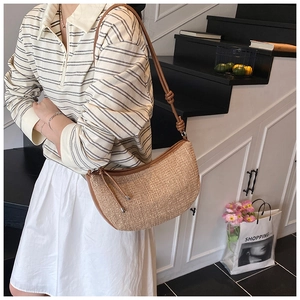 Detail of woven crescent shoulder bag with brown leather strap and knot accent