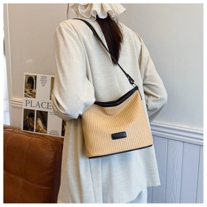 Detail of hand-woven straw shoulder bag with black leather trim and minimalist leather patch