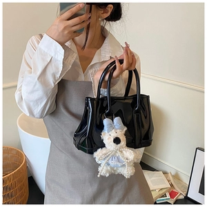 Détail du sac seau en cuir verni noir brillant avec un charmant ours en peluche blanc