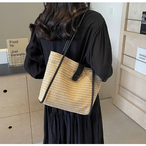 Close-up of woven straw tote bag with black leather trim and magnetic closure handle