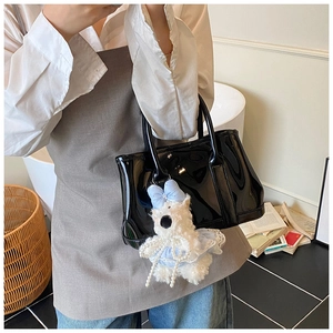Détail d'un sac seau noir brillant avec un petit ours en peluche blanc sur le côté