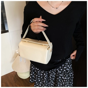 Close-up of cream textured leather handbag with gold double buckle detail and top handle