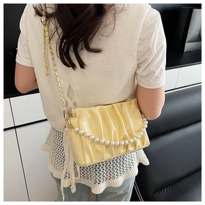 Detail view of cream pleated handbag featuring pearl handle and gold chain strap