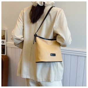 Detail of woven straw bucket bag with black leather trim and adjustable shoulder strap