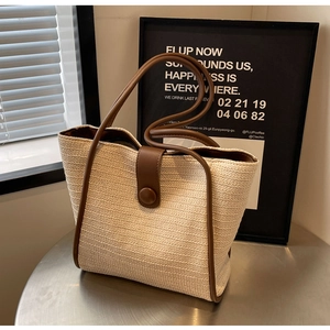 Detail of woven straw tote bag with brown leather trim on a metal table in soft light