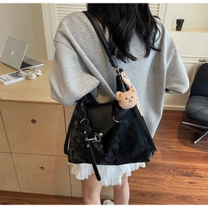 Detail of a black glossy tote bag with silver hardware and a cute plush bear pendant