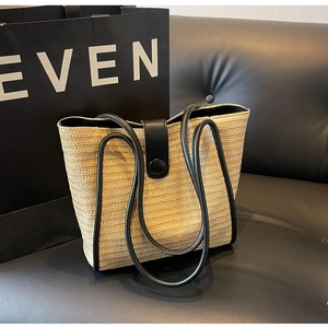 Macro shot of woven straw tote bag texture featuring black leather trim and snap closure