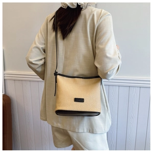 Detail of woven straw shoulder bag with black leather trim and rectangular logo patch